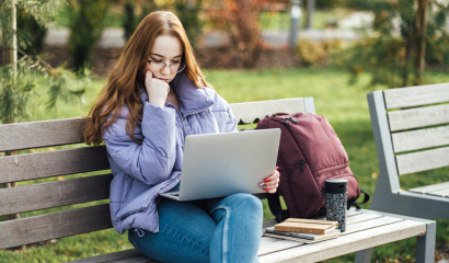 A young woman sits on a park bench, staring at her laptop screen.