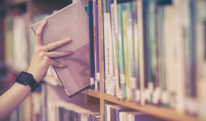 A hand is shown reaching for a book on a bookshelf.