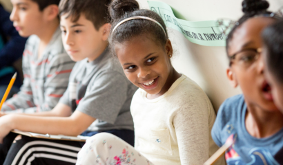 Elementary-aged school children sit and speak to each other.