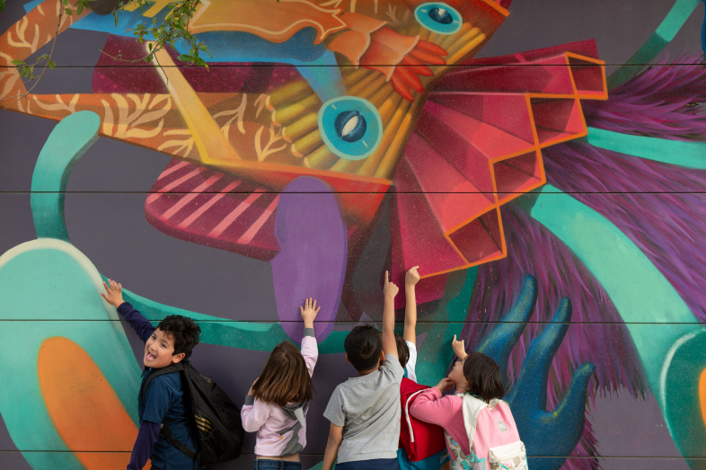 Five children touch the paint of a colorful mural.