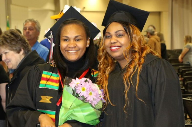 Two Black female college graduates pose side by side and smile for a photo.