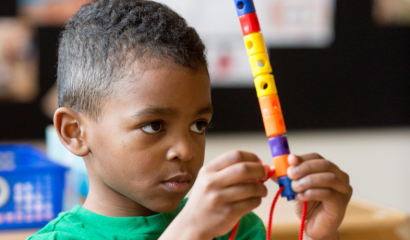 A preschool-age Black boy holds and stares at a Lego stick intently.