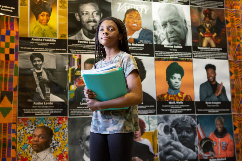 A Black girl stands in front of a Black History month display at Sutton Middle School in Atlanta. The display features iconic Black leaders, from Ida B. Wells to Aretha Franklin and Ryan Coogler.