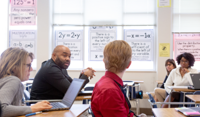 Teachers sit at desks in a classroom.